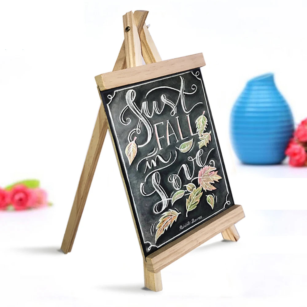 A mini wooden chalkboard easel displaying the phrase Just Fall in Love with decorative leaves.