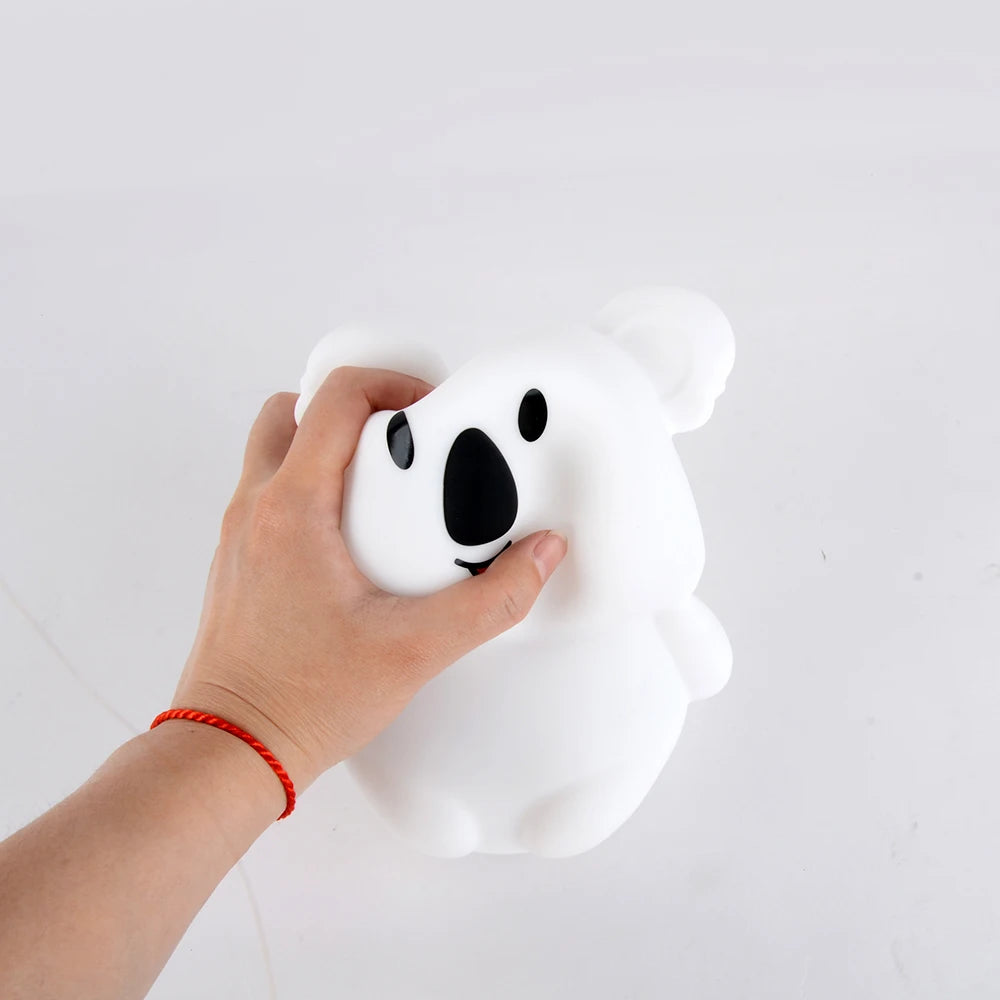 A hand is holding a white koala LED night light with a black face and ears.