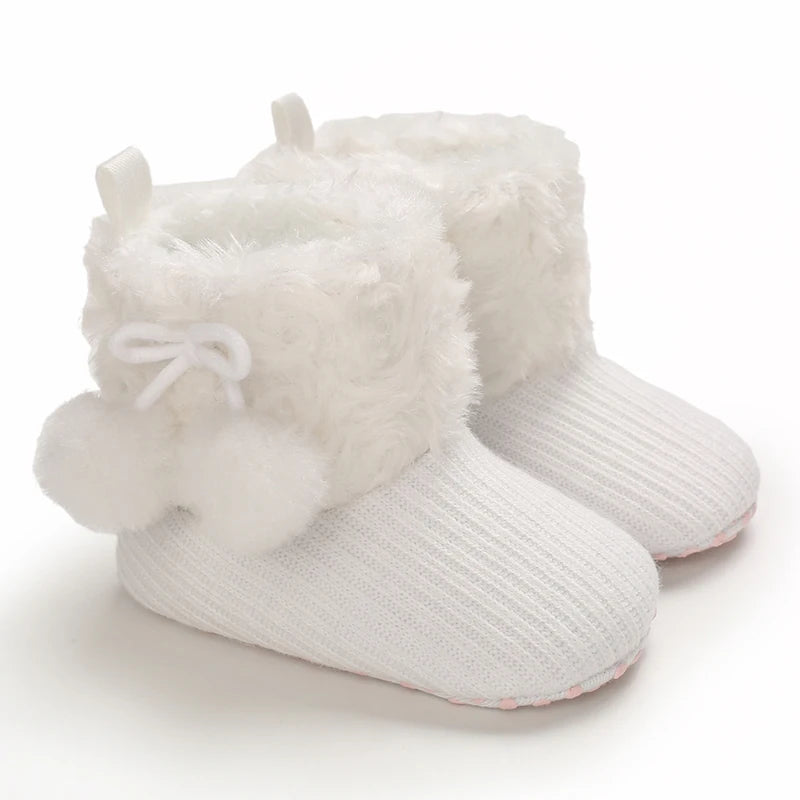 A pair of white plush baby snow boots with faux fur trim and a white bow