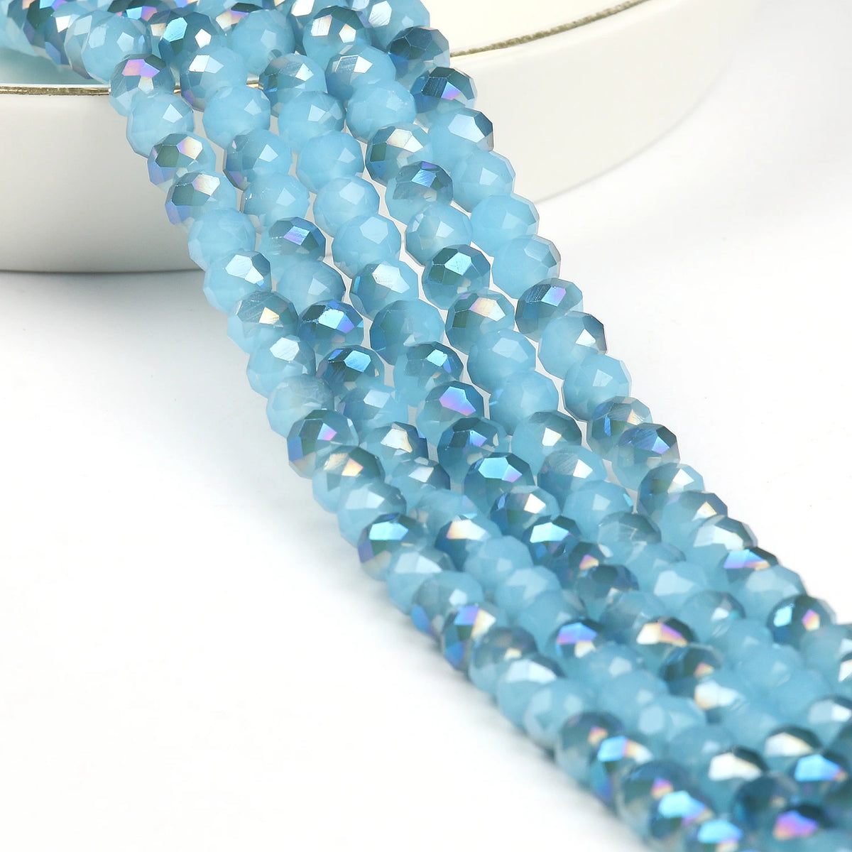 A strand of light blue faceted crystal glass beads for jewelry making laid across a white surface.