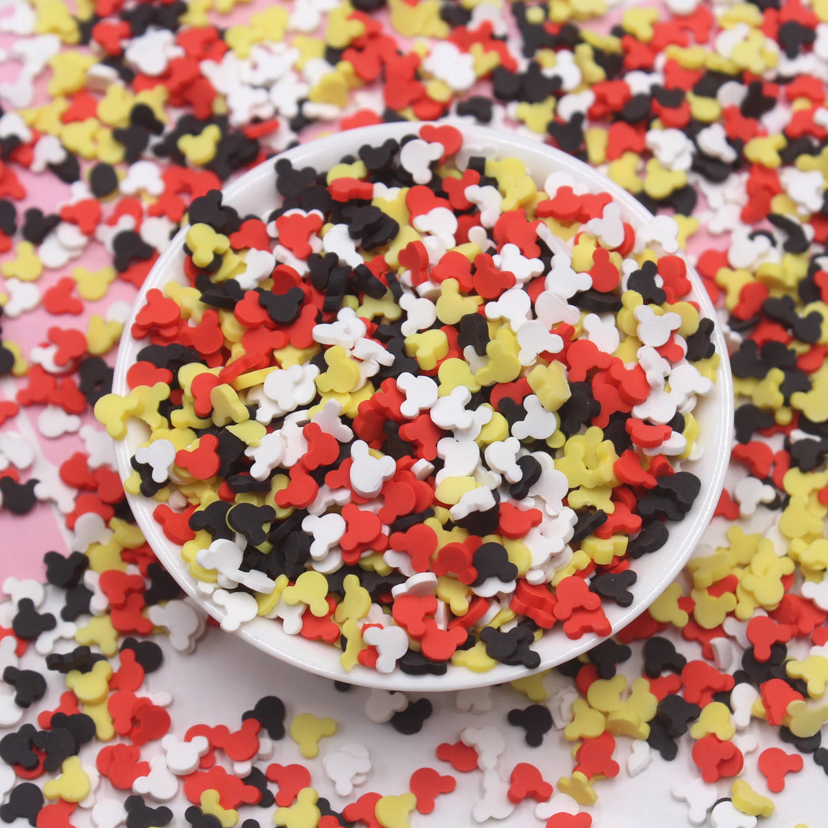 A white bowl filled with colorful cartoon polymer clay slices in red, black, yellow, and white for craft projects.