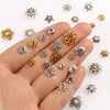 A hand displays various silver and gold Tibetan style hollow flower bead caps for jewelry making.