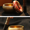 A handmade copper singing bowl and mallet resting on a dark surface.