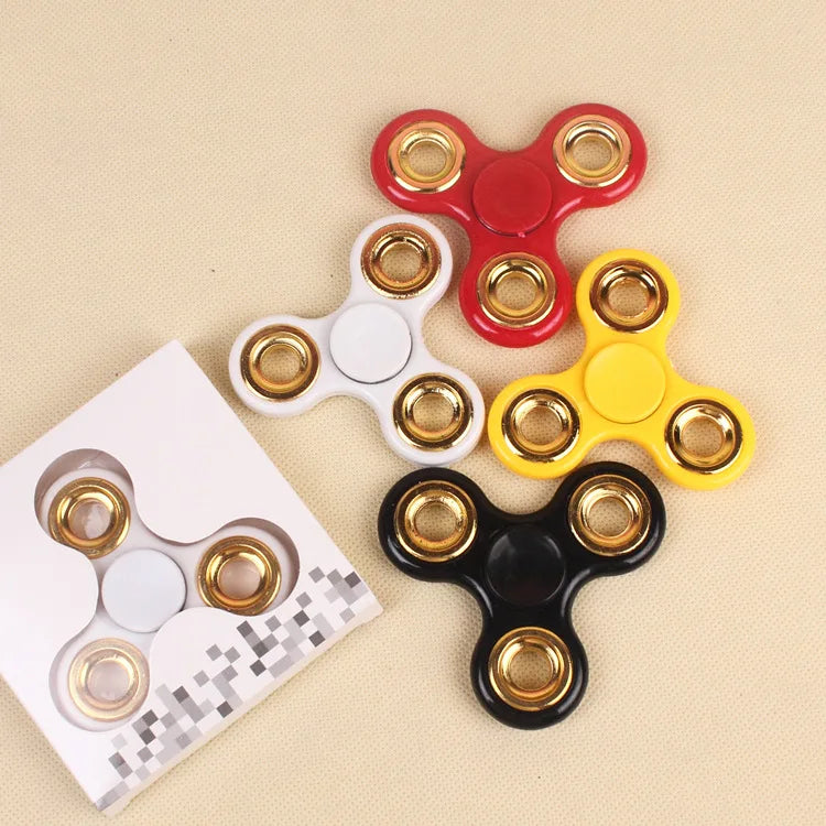 A collection of colorful ABS tri-spinner fidget toys in red, yellow, and white on a beige background.