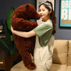 A woman is holding an oversized lifelike brown bear plush cushion in a studio setting.