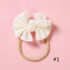 A cream-colored bow headband with a soft elastic band is displayed on a pink background.
