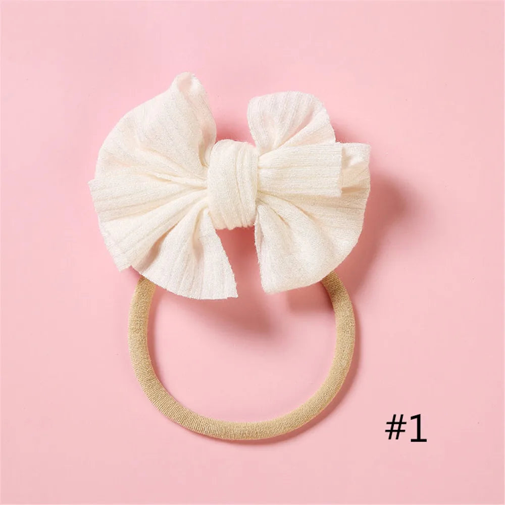 A cream-colored bow headband with a soft elastic band is displayed on a pink background.