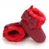 A pair of red faux fur baby first walker shoes with a bow detail.
