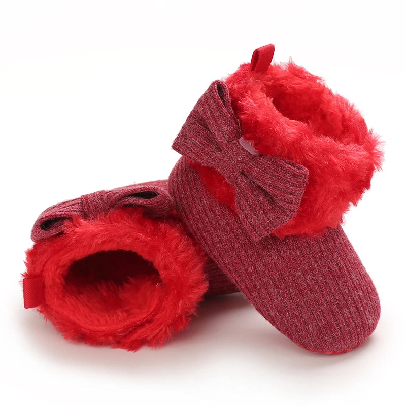 A pair of red faux fur baby first walker shoes with a bow detail.