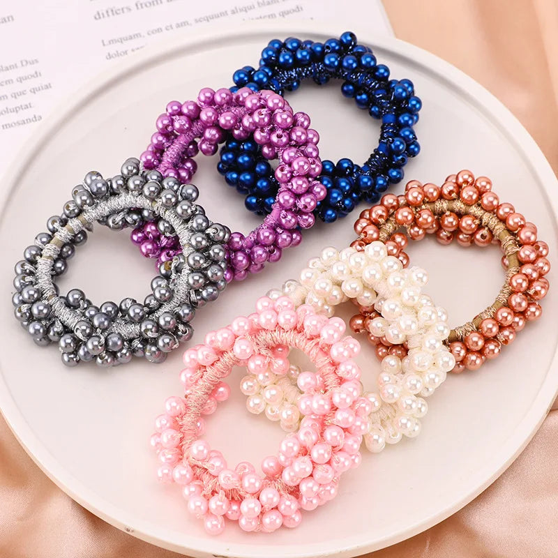 A collection of elegant pearl hair ties and bow scrunchies in various shades of blue, purple, silver, and pink arranged on a 