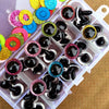 A collection of colorful plastic safety eyes in various glitter and solid colors arranged in a clear plastic tray.