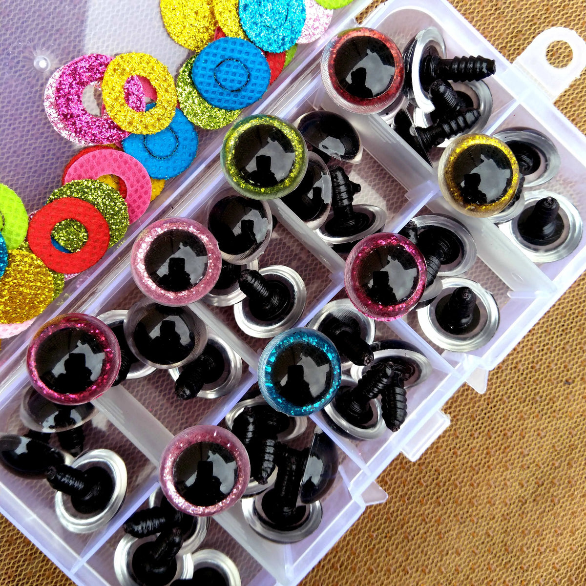 A collection of colorful plastic safety eyes in various glitter and solid colors arranged in a clear plastic tray.