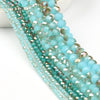 A close-up of strands of faceted crystal glass beads in shades of teal and aqua for jewelry making.
