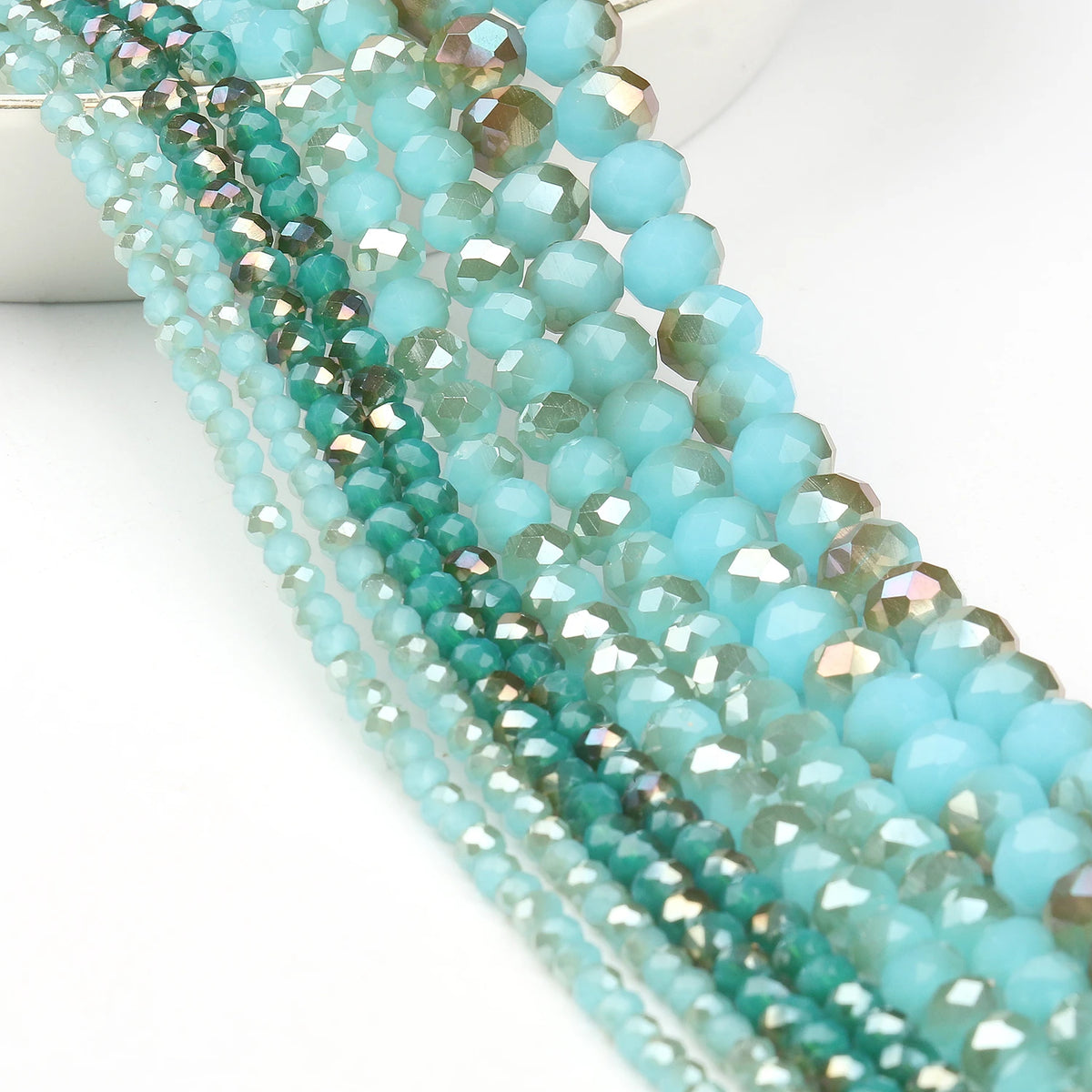A close-up of strands of faceted crystal glass beads in shades of teal and aqua for jewelry making.