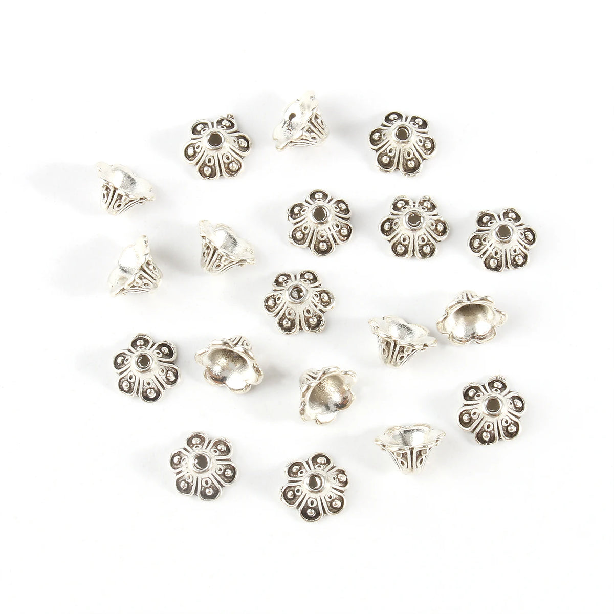 A collection of small, silver Tibetan style hollow flower bead caps for jewelry making arranged on a white background.