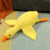 A yellow oversized kawaii goose plush pillow with orange beak and feet lying on a light blue surface.