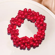 A circular arrangement of bright red pearl hair ties with bows, displayed on a white plate.
