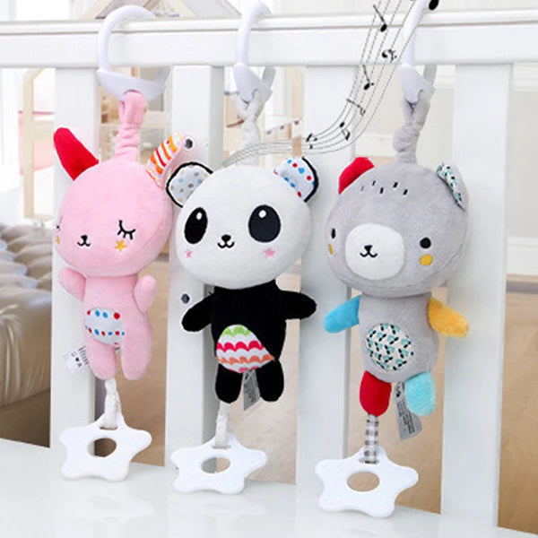 Three musical plush animal rattles in pink, black, and gray hanging from a white railing.