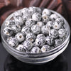 A clear glass bowl filled with small white and black floral ceramic beads for jewelry making