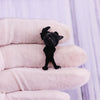 A black enamel pin shaped like a cartoon character dog is displayed on a white glove.
