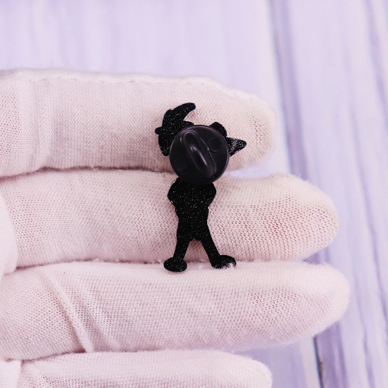 A black enamel pin shaped like a cartoon character dog is held between white gloves.