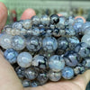 A handful of natural gemstone beads including tiger eye, lava, and turquoise in various shades are held in a hand.