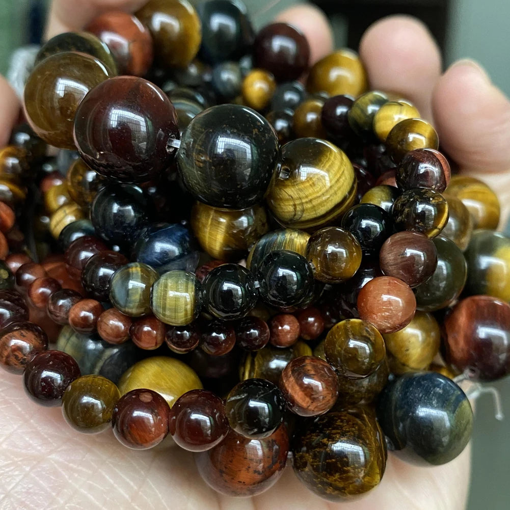 A hand holds a collection of natural gemstone beads including tiger eye, lava, and other colored stones for jewelry making.