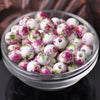 A clear glass bowl filled with small white ceramic beads decorated with pink and green floral patterns.