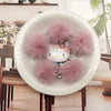 A white bowl filled with pink faux fur pom poms, displayed on a wooden table.