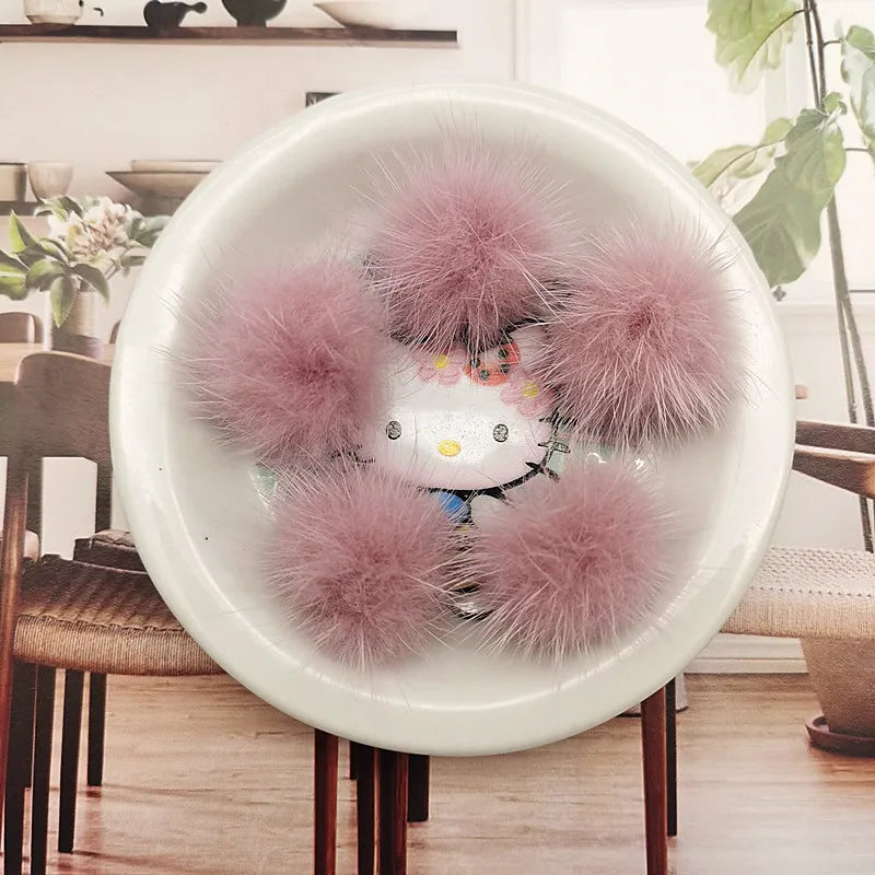 A white bowl filled with pink faux fur pom poms, displayed on a wooden table.