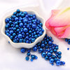 A pile of assorted blue pearl beads for jewelry making next to a pink lotus flower.