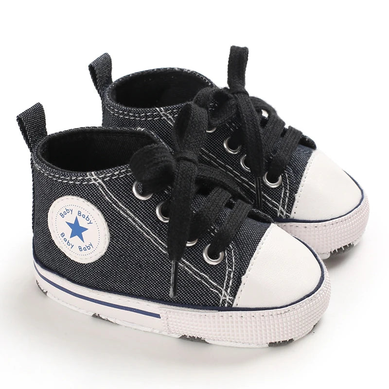 A pair of black and white canvas baby shoes with laces and studs are shown against a white background.