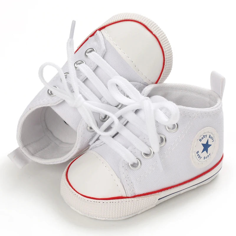 A pair of white canvas baby shoes with white laces and red trim, shown from the top view.