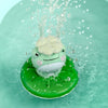 A small, light green frog bath toy with a white head is floating in clear water.