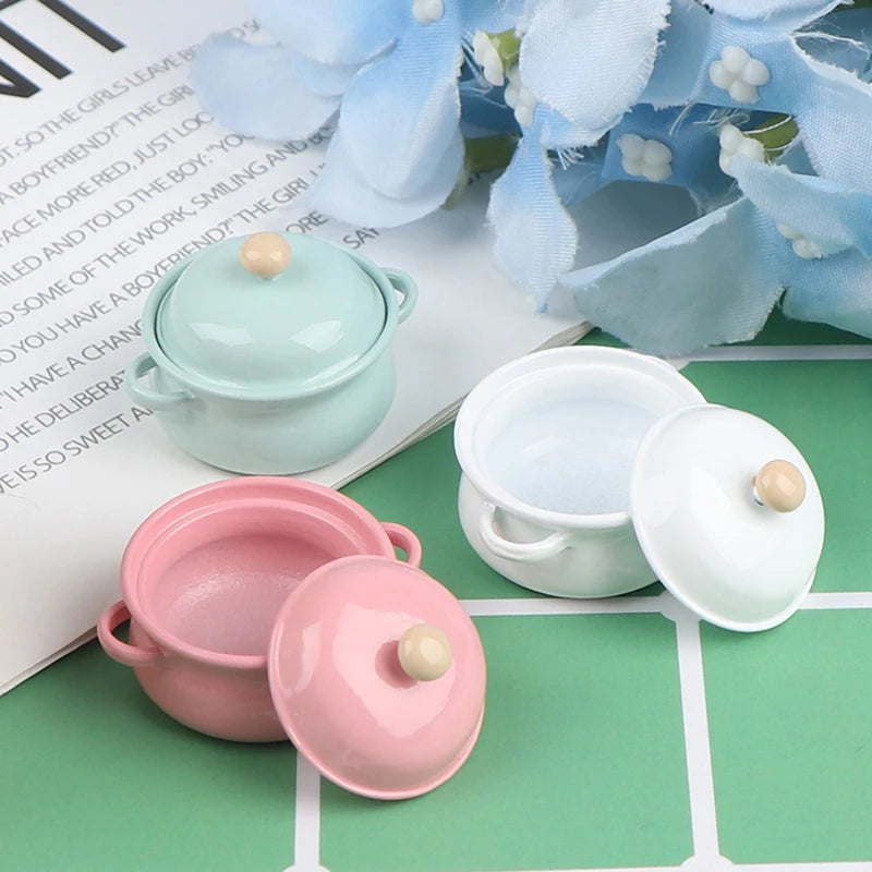 A set of miniature copper soup pots and a white teapot displayed on a green surface.