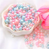 A pile of assorted pink and blue pearl beads for jewelry making, displayed in a white bowl.
