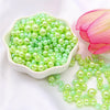 A pile of assorted light green and pale yellow pearl beads for jewelry making next to a pink lotus flower.