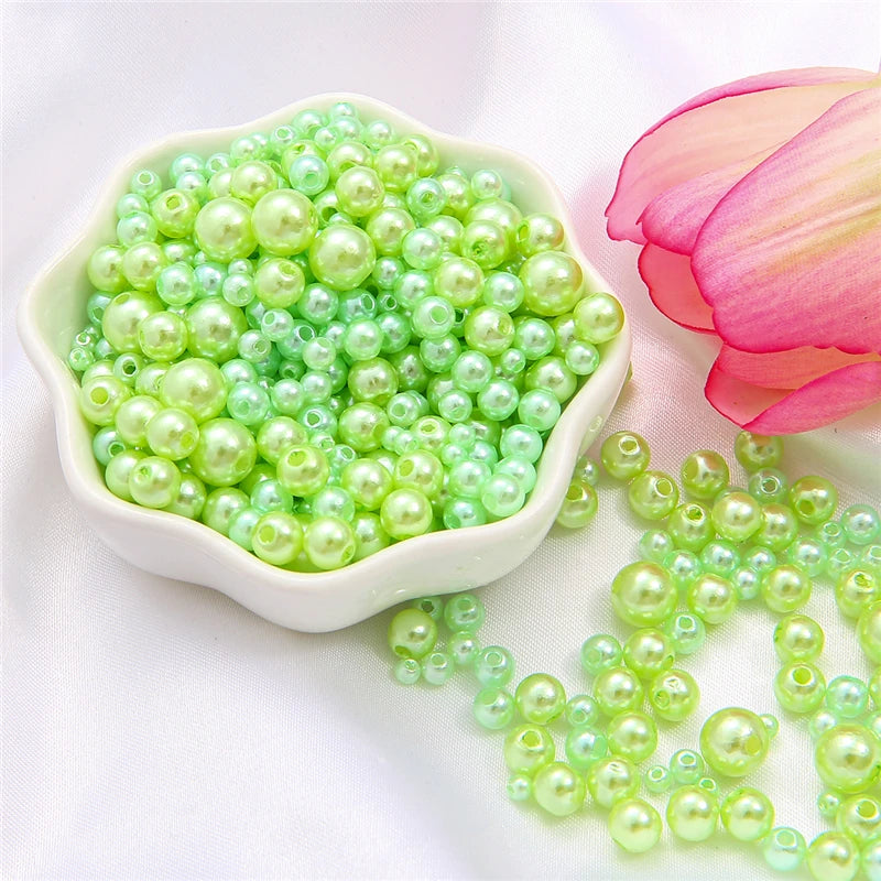 A pile of assorted light green and pale yellow pearl beads for jewelry making next to a pink lotus flower.