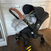 A black stroller accessory kit featuring a mosquito net, rain cover, and other items resting on a wooden floor.