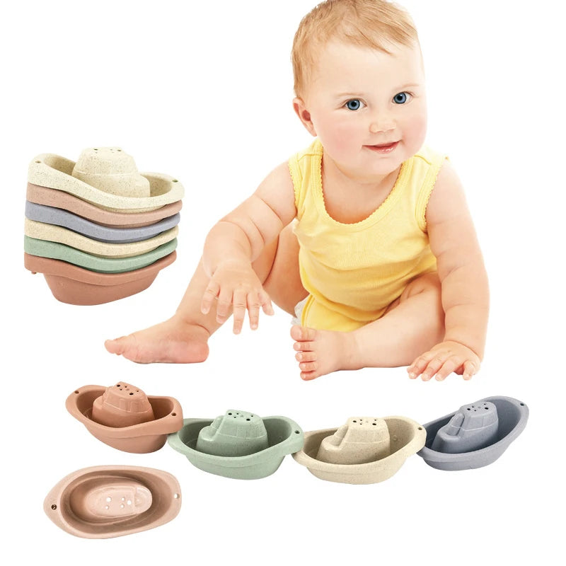 A baby is sitting and holding a set of boat-shaped stacking cups for bath time.