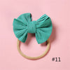 A teal knitted bow headband with a light beige elastic band against a pink background.