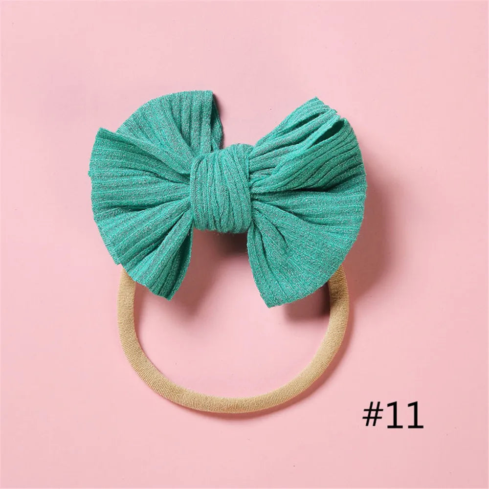A teal knitted bow headband with a light beige elastic band against a pink background.