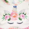 White handmade doll dress featuring a pink and green floral pattern with a unicorn design.