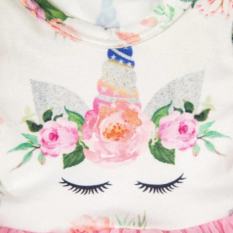White handmade doll dress featuring a pink and green floral pattern with a unicorn design.