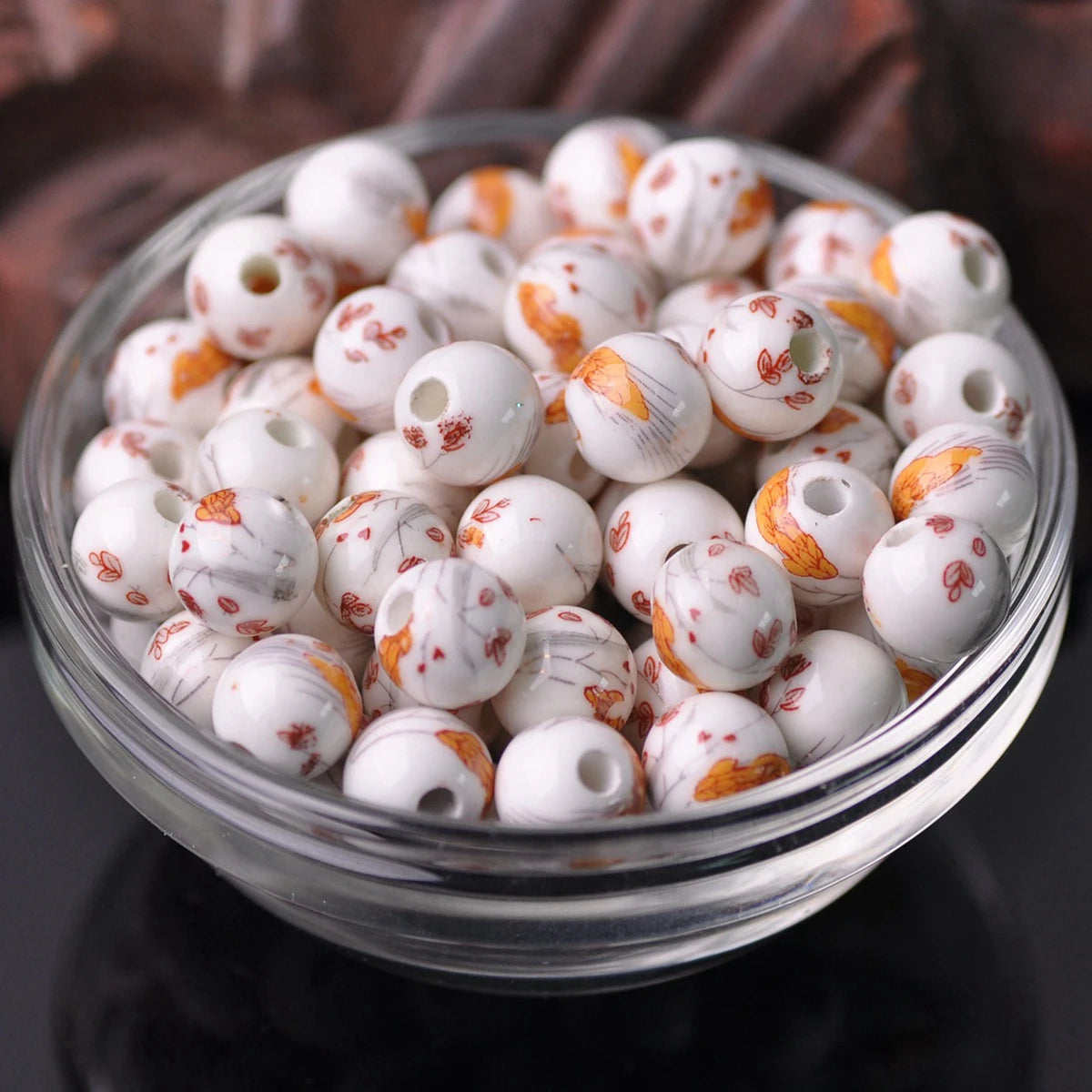 A clear glass bowl filled with small white ceramic beads decorated with orange and red floral patterns.