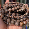 A hand holds a coil of natural gemstone beads, including tiger eye and lava stones, for jewelry making.