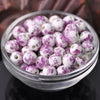 A clear glass bowl filled with small, round ceramic beads in white and purple floral patterns.