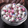 A clear glass bowl filled with pink and white floral ceramic beads for jewelry making