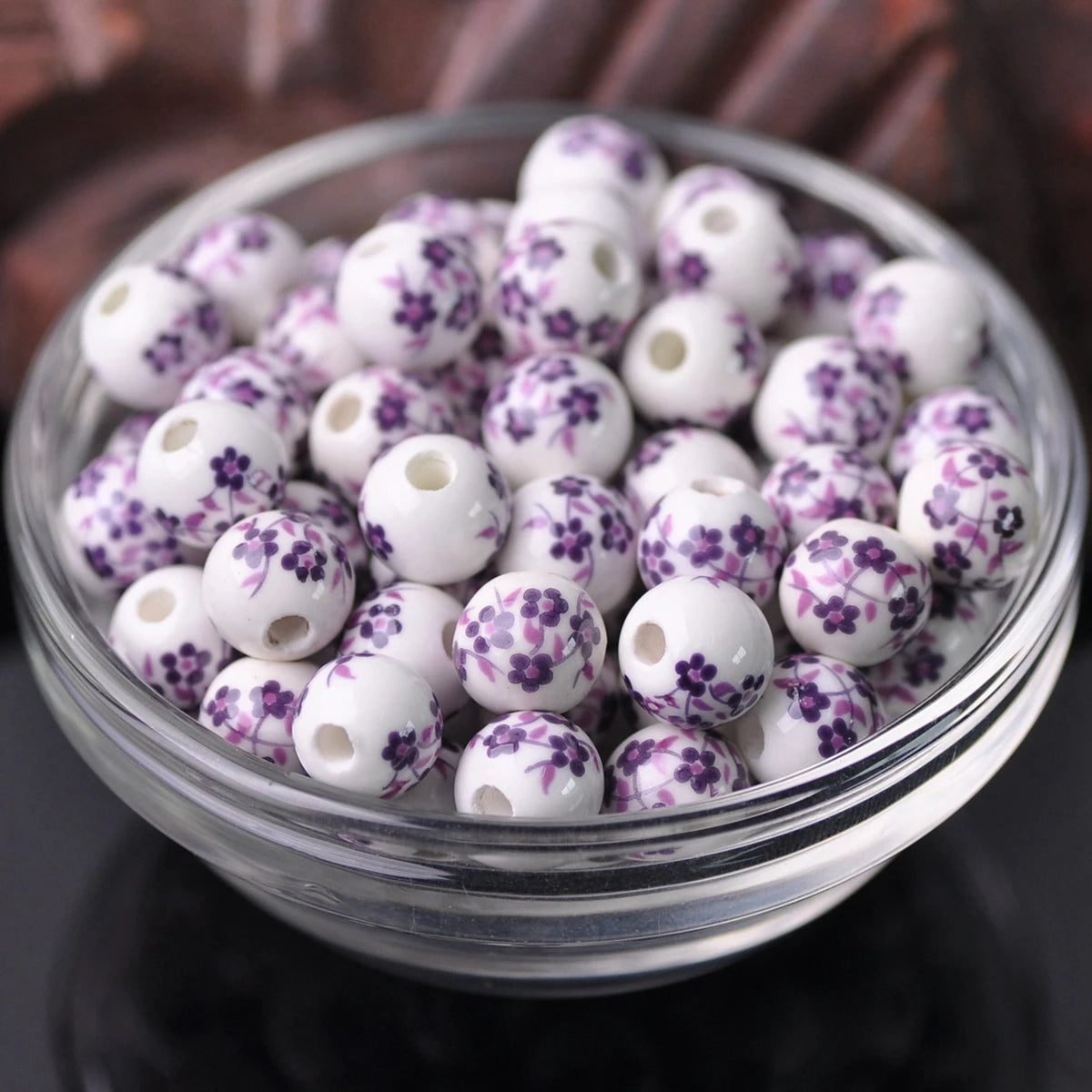 A clear glass bowl filled with small white ceramic beads decorated with purple floral patterns.