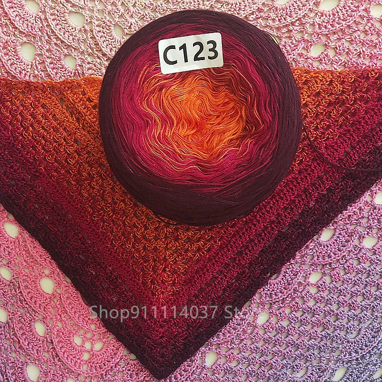 A dark purple yarn ball with an orange and pink gradient is placed on a pink knitted fabric.